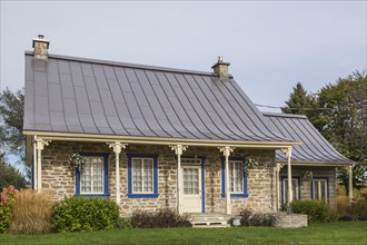 Old 1820 cottage style fieldstone house facade with blue trim and brown standing seam sheet metal roof plus stacked log extension in autumn