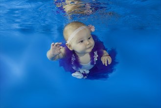 Baby girl dressed as a ballet dancer swimming under water in a pool