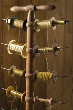 Thread stand in front of wooden wall with various gold and yellow yarns