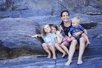 Mother and three toddlers sitting on rocks