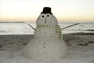 Snowman made of sand on the beach in the evening light