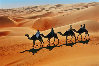 Tourists on camel ride in front of high sand dunes