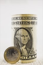 Rolled US one dollar bill standing upright and one Euro coin on white textured background