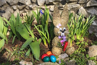 Easter bunny made of straw and colorful dyed Easter eggs in the flower bed