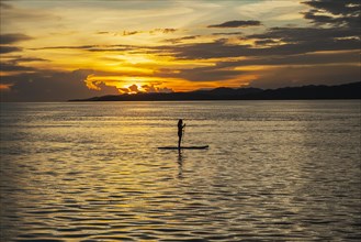 Woman on standup paddle board in the sea at sunset