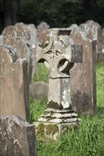 Celtic cross between old grave stones in cemetery