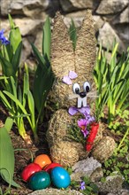 Easter bunny made of straw and colorful dyed Easter eggs in the flower bed