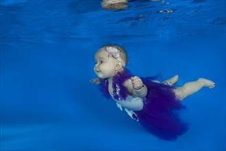 Baby girl dressed as a ballet dancer swimming underwater in a pool