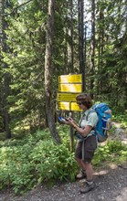 Female hiker at signpost in forest reads map on GPS device