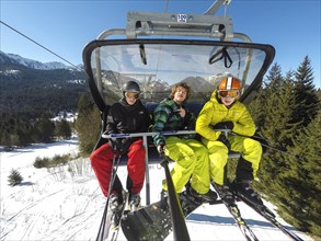 Three teenagers on chairlift with skis and snowboard