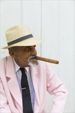 Aged Cuban man with straw hat smokes cigar