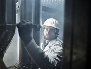 Mechanic with white helmet and lab coat moving a lever of a refrigerant line