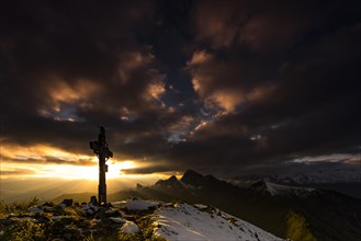 Cross on the summit of Zafernhorn at sunrise with dark clouds