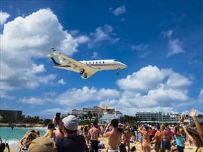 Tourists watching and photographing an airplane landing over Maho Beach