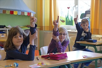 Students in elementary school with raised hands in classroom