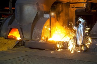 A steel worker in a protective suit taking a 1500 hot raw iron sample at the tapping