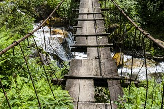 Old wooden suspension bridge across small river in Upper Modi Khola valley