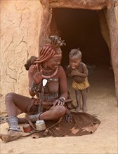 Himba woman with child in front of the mud hut