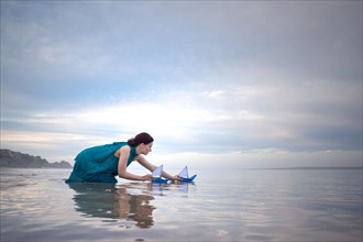 Woman with blue paper ships at low tide on the beach