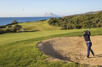 Golfer hitting from bunker at La Alcaidesa Golf Resort with Mediterranean Sea and Rock of Gibraltar