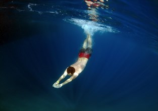 Man swims underwater in clear blue water