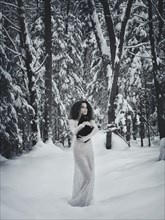 Beautiful woman in white long dress walking in the snow with a black cat in her hands