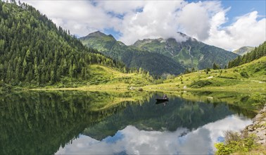 Fisherman on Lake Riesachsee with reflection of forest and mountains