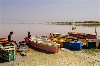 Two young women sitting on colourful wooden boats at Lac Rose