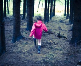 Young girl in pink coat running towards light out of forest
