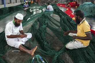 Local men repairing fishing nets in hall at harbour