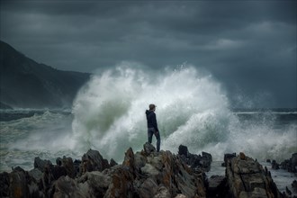 Man on rock in front of breaking wave