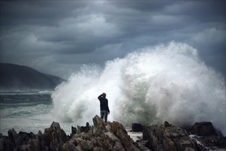Man on rock in front of breaking wave