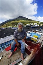 Fisherman in his boat in front of volcano on Scari beach