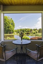 View of pond and screened wooden gazebo from sunroom with bistro table and wicker seat arcmchairs inside a 1990s contemporary Victorian style country home