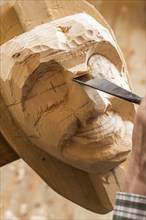 Carving the face of a wooden mask into wooden block using wood carving tools
