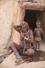 Himba woman with child in front of the mud hut