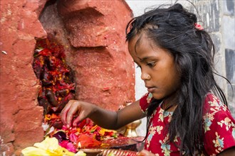 Little girl offering Prasad to statues of gods outside Khadga Devi Temple