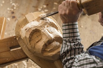 Carving the face of a wooden mask into wooden block using wood carving tools