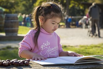 Eurasian girl sitting at wooden table with chestnuts