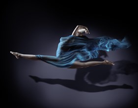 Beautiful woman in mid-air with flowing blue cloth wrapping her nude body