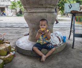 Little Indonesian boy eating grilled corn on the road side