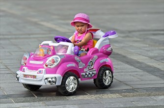 Little girl with frowning face rides in electric toy car