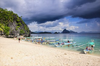 Outrigger boats before a storm anchoring on a sandy beach in the Bacuit archipelago