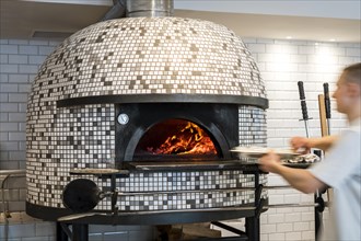 Man putting a pizza into modern Italian pizza stove