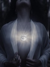 Young woman wearing a magical full moon pendant glowing on her bare chest