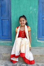 Smiling Nepalese girl seated on steps in front of a colorful house