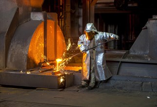 A steel worker in a protective suit taking a 1500 hot raw iron sample at the tapping