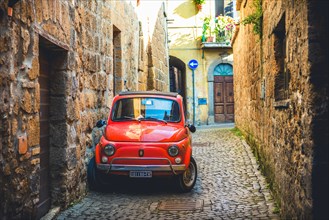 Old red Fiat 500 parked in a narrow alley
