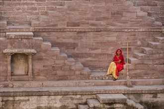 Woman in colorful sari resting on the steps at Toorji Ka Jhalara