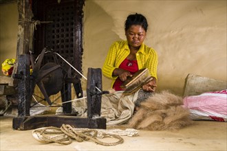 Native woman spinning sheep's wool with traditional spinning wheel in front of house